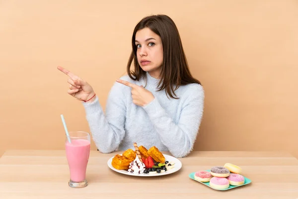 Adolescente Chica Comiendo Gofres Aislados Sobre Fondo Beige Asustado Señalando —  Fotos de Stock