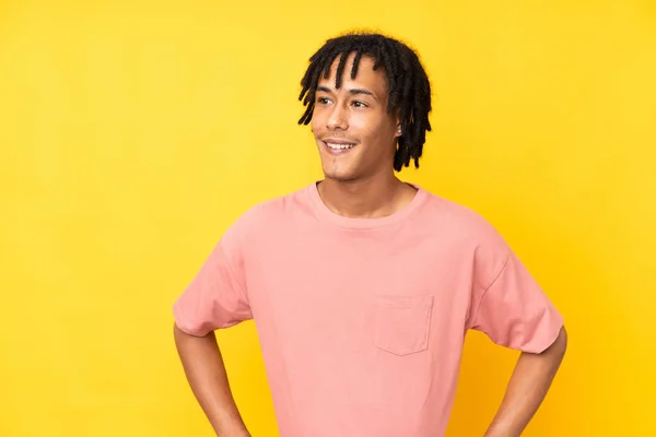 若いアフリカ系アメリカ人の男は腰と笑顔で腕をポーズ黄色の背景に隔離 — ストック写真