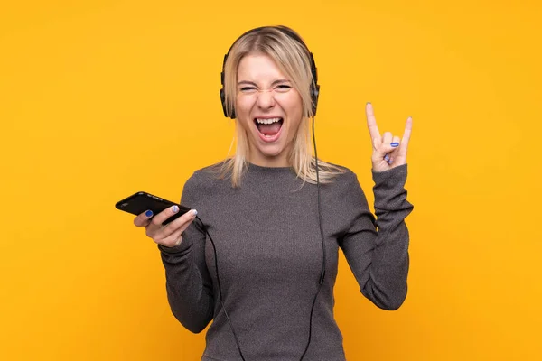 Young Blonde Woman Isolated Yellow Background Listening Music Mobile Making — 스톡 사진