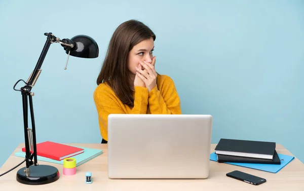 Student girl studying in her house isolated on blue background covering mouth and looking to the side