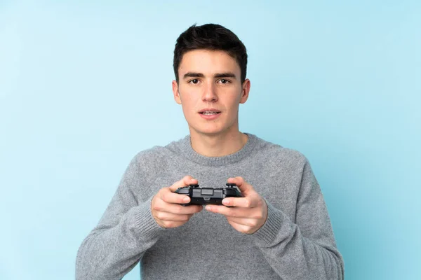 Adolescente caucásico hombre jugando con un controlador de videojuegos aislado sobre fondo azul —  Fotos de Stock