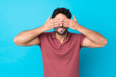 Sakallı, genç, yakışıklı, soyutlanmış, mavi arka planda, gözleri elle kaplanmış.