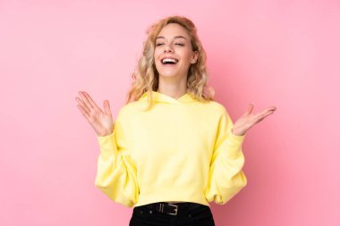Pembe arka planda izole edilmiş sweatshirt giyen genç sarışın kadın çok gülümsüyor.