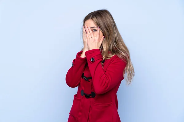 若いです女性とともに冬コート上の隔離された青の背景カバー目と見透かし指 — ストック写真