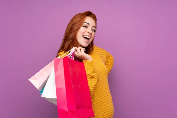 赤毛ティーン女の子上の隔離された紫背景を保持ショッピングバッグと笑顔 — ストック写真