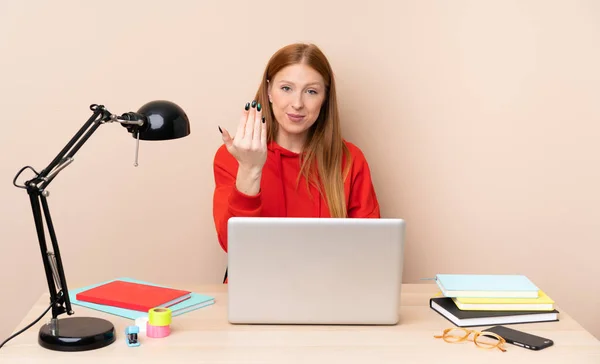 Young student woman in a workplace with a laptop inviting to come with hand. Happy that you came