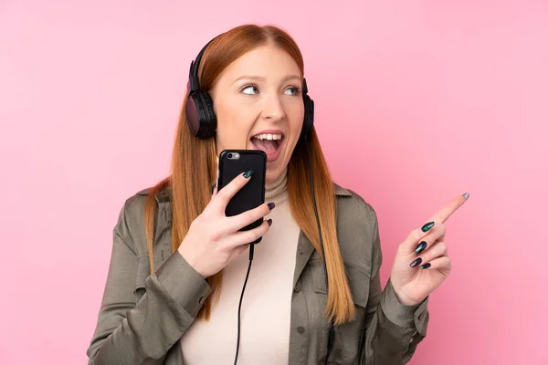 Jeune Rousse Femme Sur Fond Rose Isolé Écoutant Musique Avec — Photo