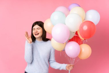 Genç Ukraynalı kız izole edilmiş pembe arka planda bir sürü balon tutuyor ve gülüyor.