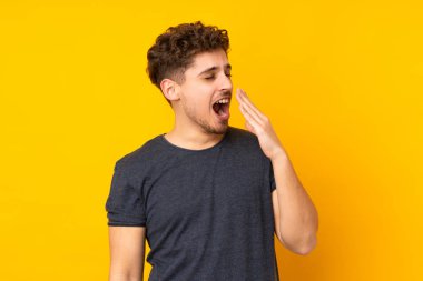 Kafkasyalı genç adam arka planı izole etti esneyerek ve ağzını eliyle açık tutarak.