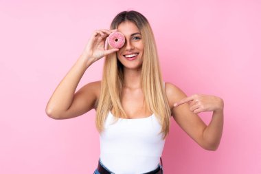 Genç Uruguaylı kadın izole pembe arka planda elinde donut ve mutlu.