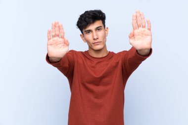 Arjantinli genç adam izole edilmiş mavi arka planda durma hareketi yapıyor ve hayal kırıklığına uğruyor.