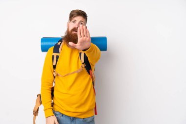 İzole edilmiş beyaz arka planda büyük bir sırt çantası olan dağcı genç adam eliyle durdurma hareketi yapıyor.