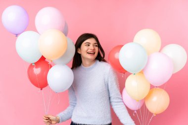 Genç Ukraynalı kız pembe arka planda bir sürü balon tutuyor.