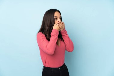 Genç melez kadın mavi arka planda izole edilmiş ağzını kapatıyor ve yan tarafa bakıyor.