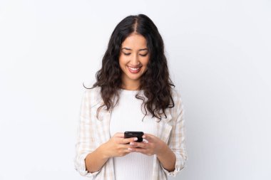 İzole edilmiş beyaz arka planda melez bir kadın cep telefonuyla mesaj gönderiyor.