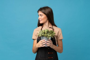 Soyutlanmış mavi arka planda bir saksı alan genç bir kadın.