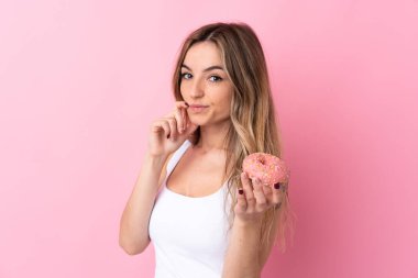 Soyutlanmış pembe arka planı olan genç bir kadın elinde donut tutuyor.
