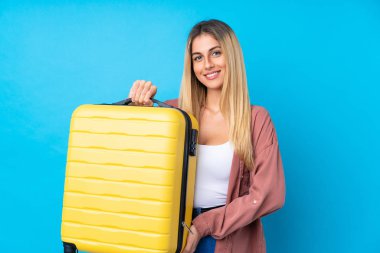 Genç Uruguaylı kadın izole edilmiş mavi arka planda seyahat valiziyle tatilde.
