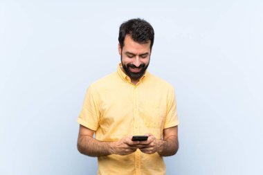 Mavi arka planda sakallı genç bir adam cep telefonuyla mesaj gönderiyor.