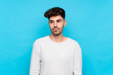 Soyutlanmış mavi arka planda genç bir adam şüpheli hareketler yapıyor.