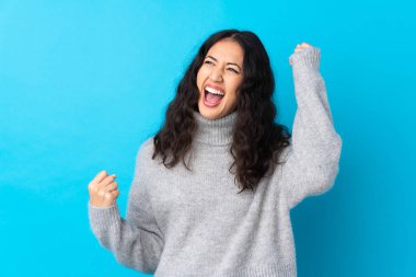 İspanyol Çinli kadın mavi arka planda zaferi kutluyor.