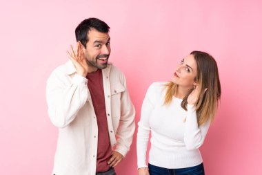 Sevgililer Günü 'nde bir çift pembe arka planda bir şeyler dinlerken elini kulağına koyar.