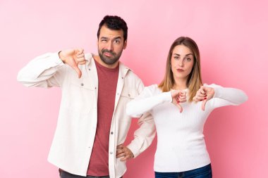Sevgililer Günü 'ndeki çift pembe arka planda iki eliyle baş parmağının aşağıda olduğunu gösteriyor.
