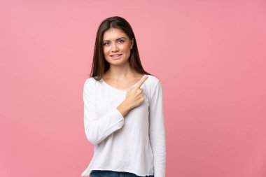 Soyutlanmış pembe arka planı olan genç bir kadın bir ürünü sunmak için kenarı işaret ediyor.