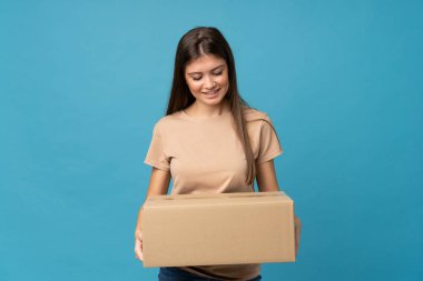 İzole edilmiş mavi arka plan üzerinde genç bir kadın başka bir yere taşımak için bir kutu tutuyor.