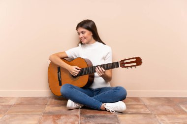 Gitarlı genç bir kadın yerde oturmuş gülüyor.