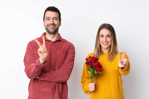 情人节的情侣们抱着鲜花 在孤独的背景上微笑着 并展示胜利的标志 — 图库照片