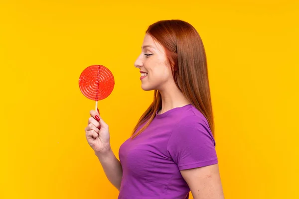 Jovem ruiva segurando um pirulito sobre fundo amarelo — Fotografia de Stock