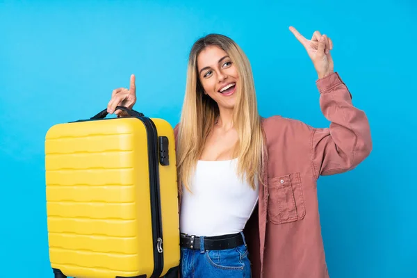 年轻的乌拉圭女人带着旅行箱和指点度假时带着蓝色的背景 — 图库照片