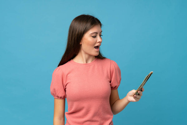 Young woman over isolated blue background taking a lot of money