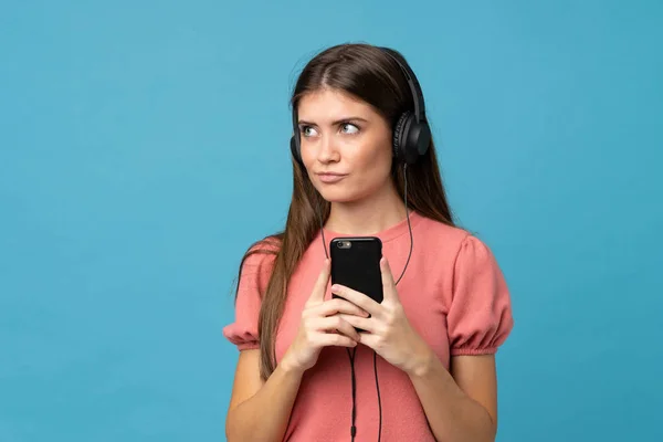 Jovem Mulher Sobre Fundo Azul Isolado Usando Celular Com Fones — Fotografia de Stock