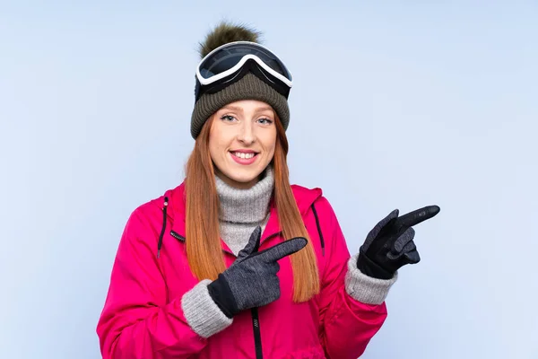 Lyžařka Ryšavá Žena Snowboardovými Brýlemi Přes Izolovanou Modrou Stěnu Ukazující — Stock fotografie