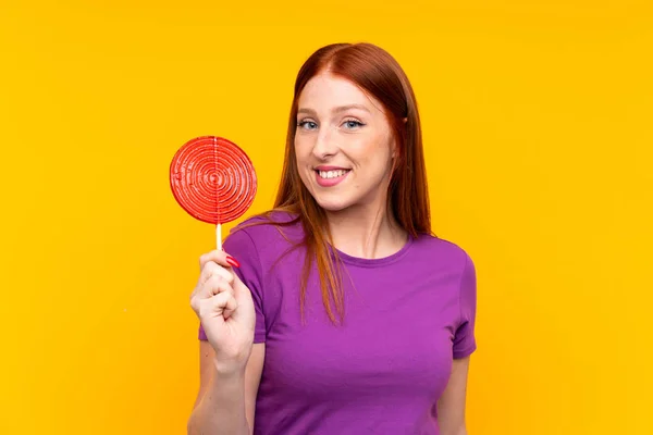 Jonge roodharige vrouw met een lolly over gele achtergrond — Stockfoto