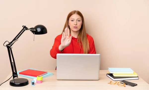 Young student woman in a workplace with a laptop making stop gesture