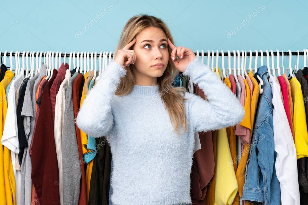 Teenager Russian girl buying some clothes isolated on blue background having doubts and thinking