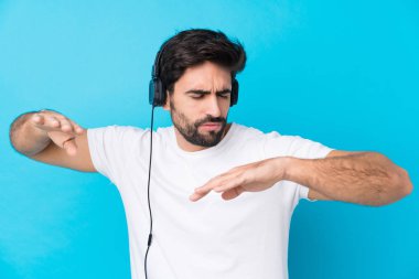 Mavi arka planda sakallı yakışıklı genç adam müzik ve dans dinliyor.