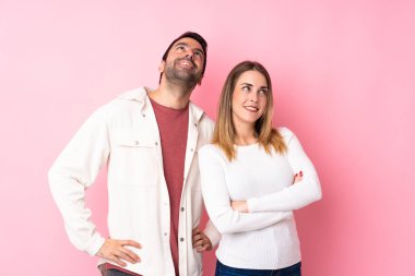 Sevgililer Günü 'nde bir çift pembe arka planda gülümserken yukarı bakıyor.