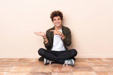 Kafkasyalı genç bir adam yerde oturuyor ve bir ilan vermek için fotokopi makinesini avucunun içinde tutuyor.