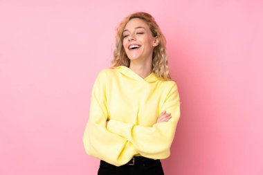 Pembe arka planda izole edilmiş kazak giyen genç sarışın kadın mutlu ve gülümsüyor.