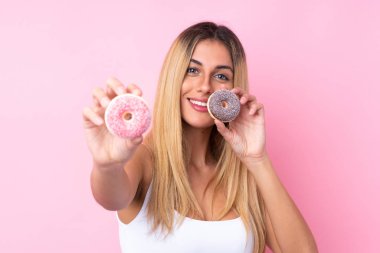 Genç Uruguaylı kadın pembe arka planda mutlu bir ifadeyle donut tutuyor.