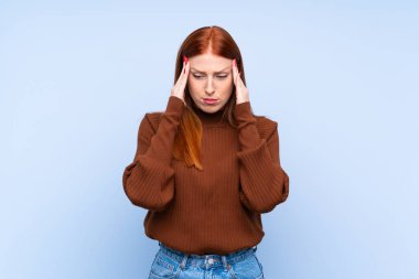Genç kızıl saçlı kadın mavi arka planda, baş ağrısı var.