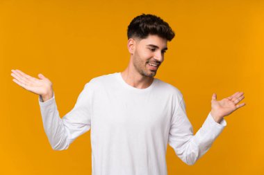 İzole edilmiş turuncu arka planı olan genç bir adam iki eliyle kopyalama alanını tutuyor.