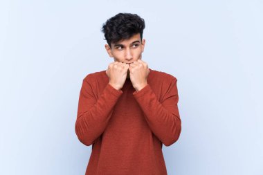 Arjantinli genç adam izole edilmiş mavi arka planda gergin ve korkmuş bir şekilde elleriyle suni teneffüs yapıyor.