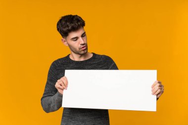 İzole edilmiş arka planı olan genç bir adam bir konsept eklemek için boş beyaz bir levha tutuyor.