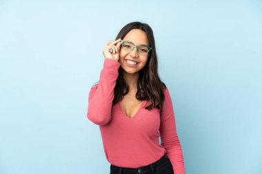 Mavi arka planda, gözlüklü ve mutlu, melez bir kadın.