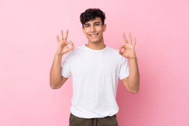 Arjantinli genç adam izole edilmiş pembe arka planda parmaklarıyla tamam işareti gösteriyor.